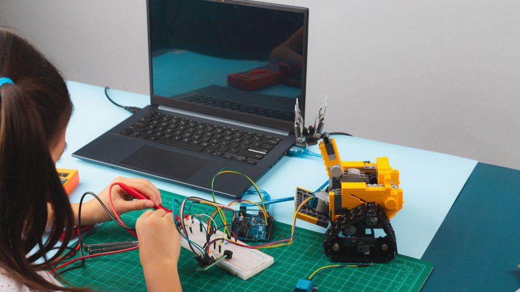 A child working on a robotics project with wires connected to a circuit board and a laptop